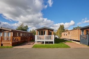A row of wooden mobile homes with a central white deck and a paved walkway. - Host & Stay | Butterfly Retreat (Northumberland)