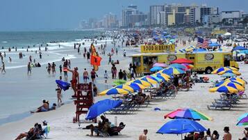 A crowded beach with umbrellas and beach chairs, a lifeguard tower, and a food truck.