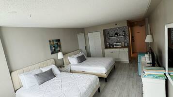 A bedroom with two beds, a desk, a chair, and a kitchenette.