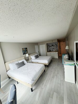 Een slaapkamer met twee bedden, een bureau, een stoel en een kitchenette.