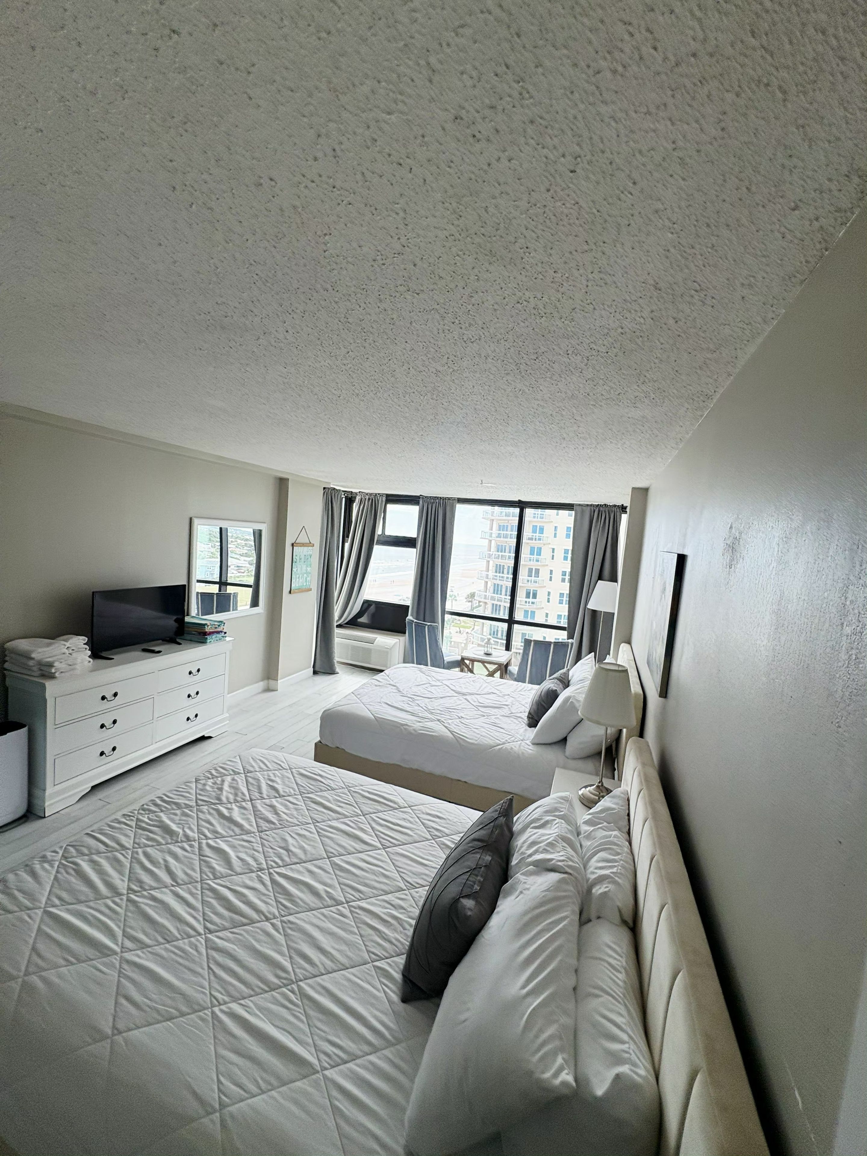 Ein Hotelzimmer mit einem großen Bett, einem Fernseher, einem Schminktisch und einem Fenster mit Vorhängen.