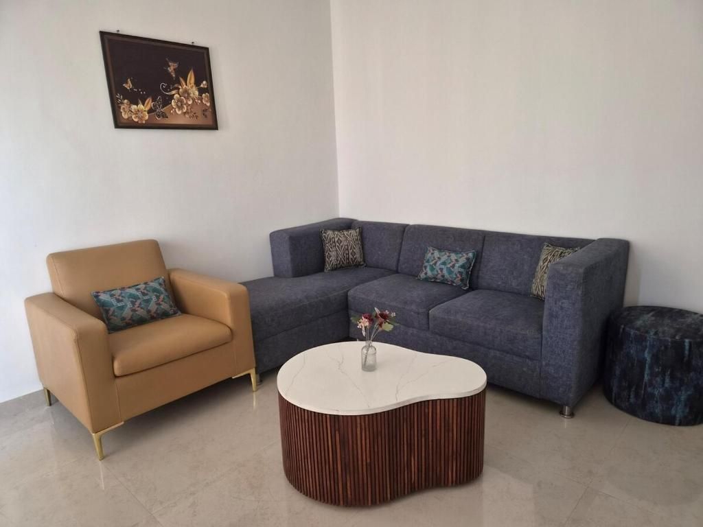 A living room with a brown leather armchair, a grey sectional sofa, and a round coffee table with a vase of flowers.