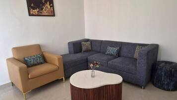 A living room with a brown leather armchair, a grey sectional sofa, and a round coffee table with a vase of flowers.