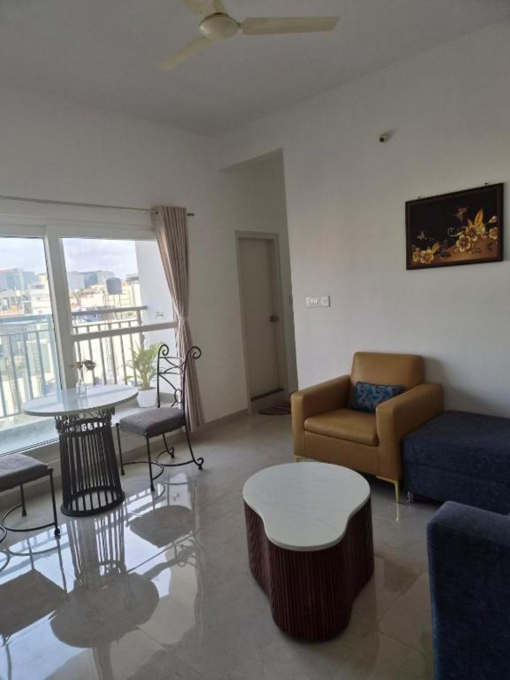 A modern living room with a balcony, a round table, a sofa, and a painting on the wall.