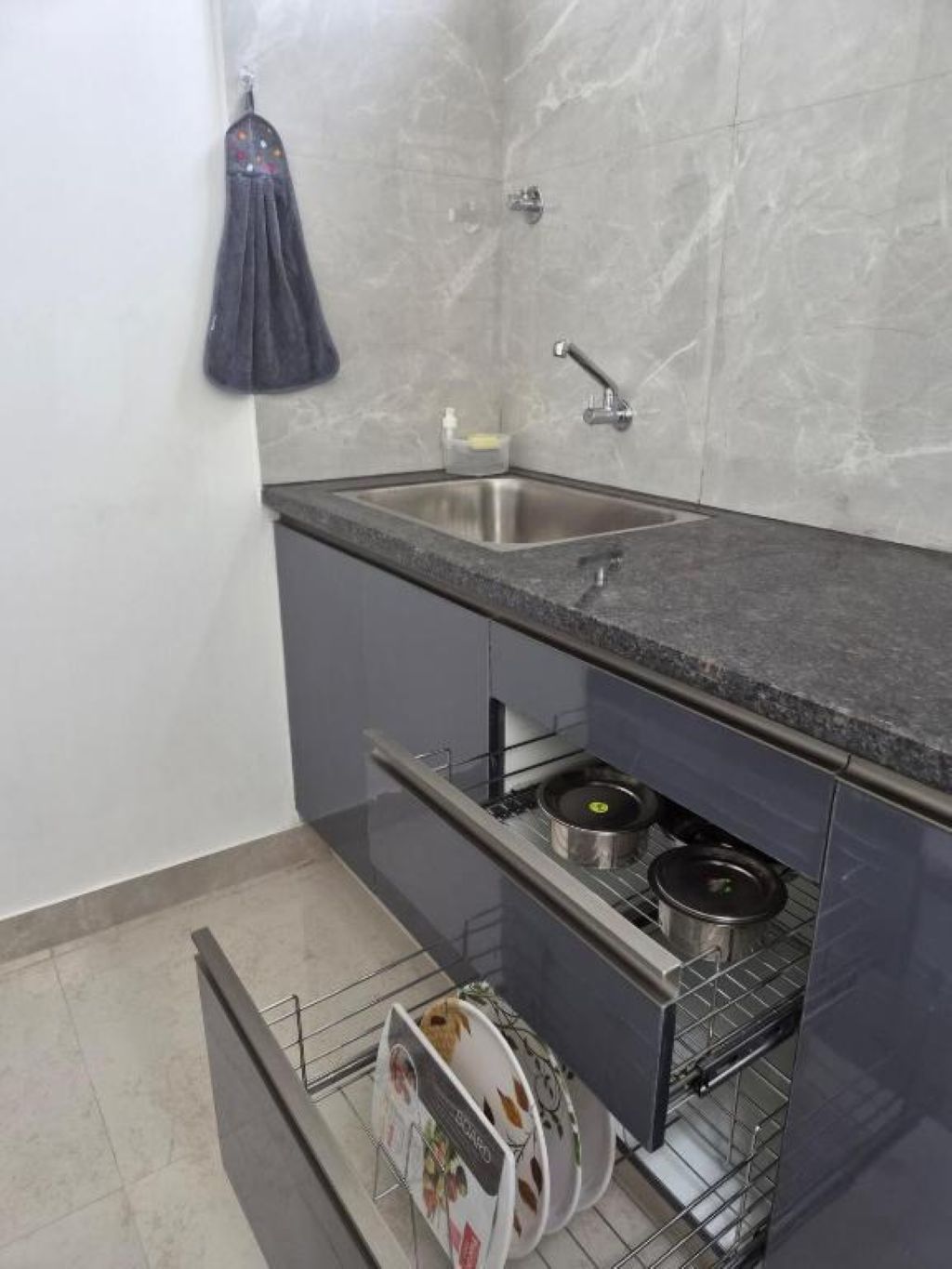 A kitchen with a stainless steel sink, a towel hanging on the wall, and a dish rack with plates.