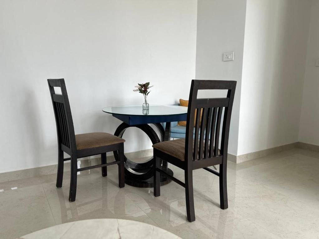 A dining area with a round table and two chairs, a vase with flowers, and a light-colored floor.