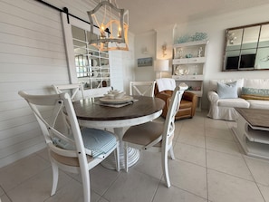 A dining area with a round table, white chairs, and a chandelier. - Gulf & Pool Views • Private Beach Access • Walk to Shops & Restaurants in Marco (Marco Island)