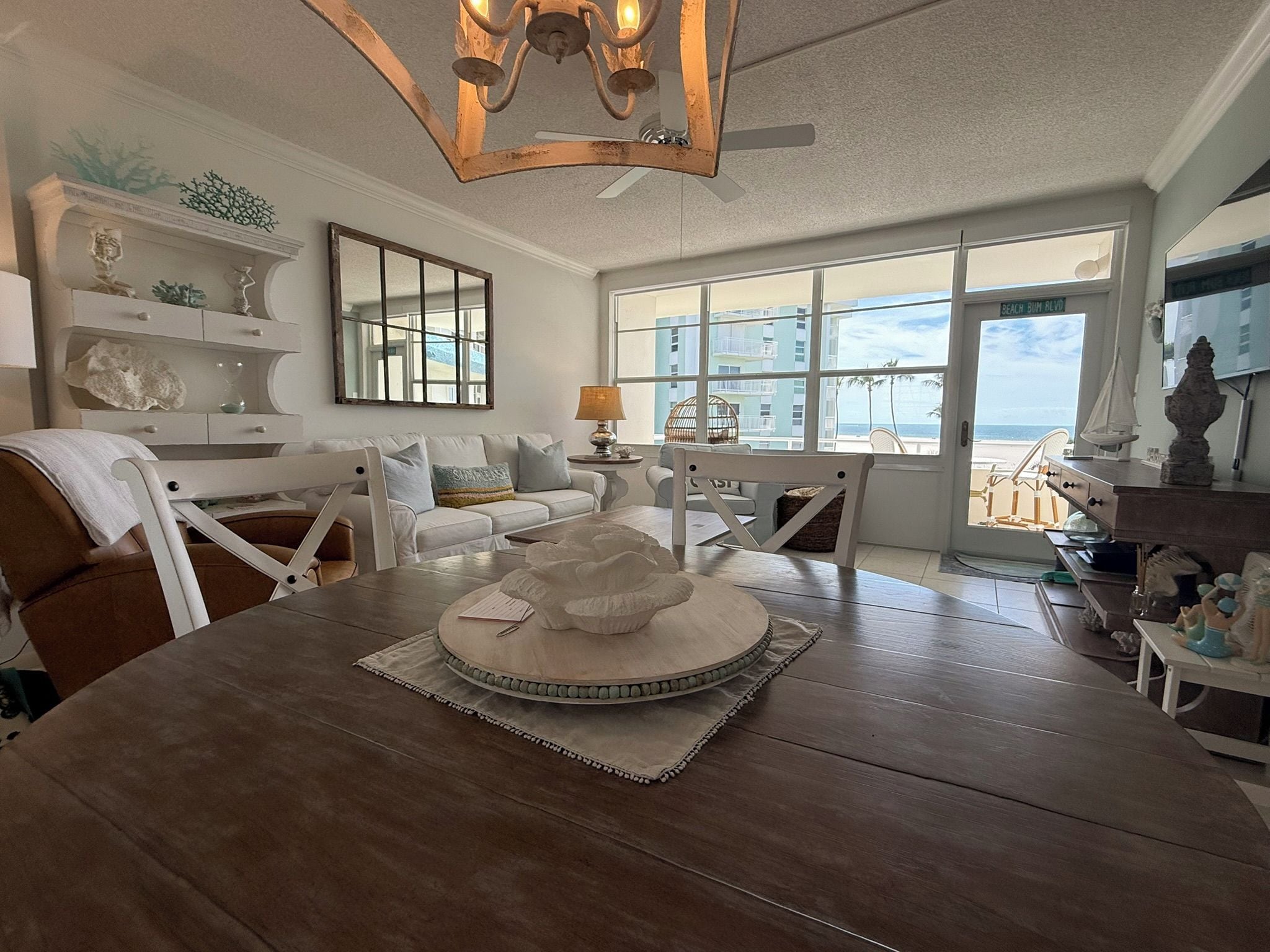 Un salon spacieux avec une grande table à manger en bois, des sièges confortables, un élément décoratif central et une vue sur l’océan grâce à de grandes fenêtres.