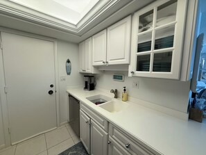 A kitchen with white cabinets, a built-in dishwasher, a coffee maker, and a sink with a soap dispenser. - Gulf & Pool Views • Private Beach Access • Walk to Shops & Restaurants in Marco (Marco Island)