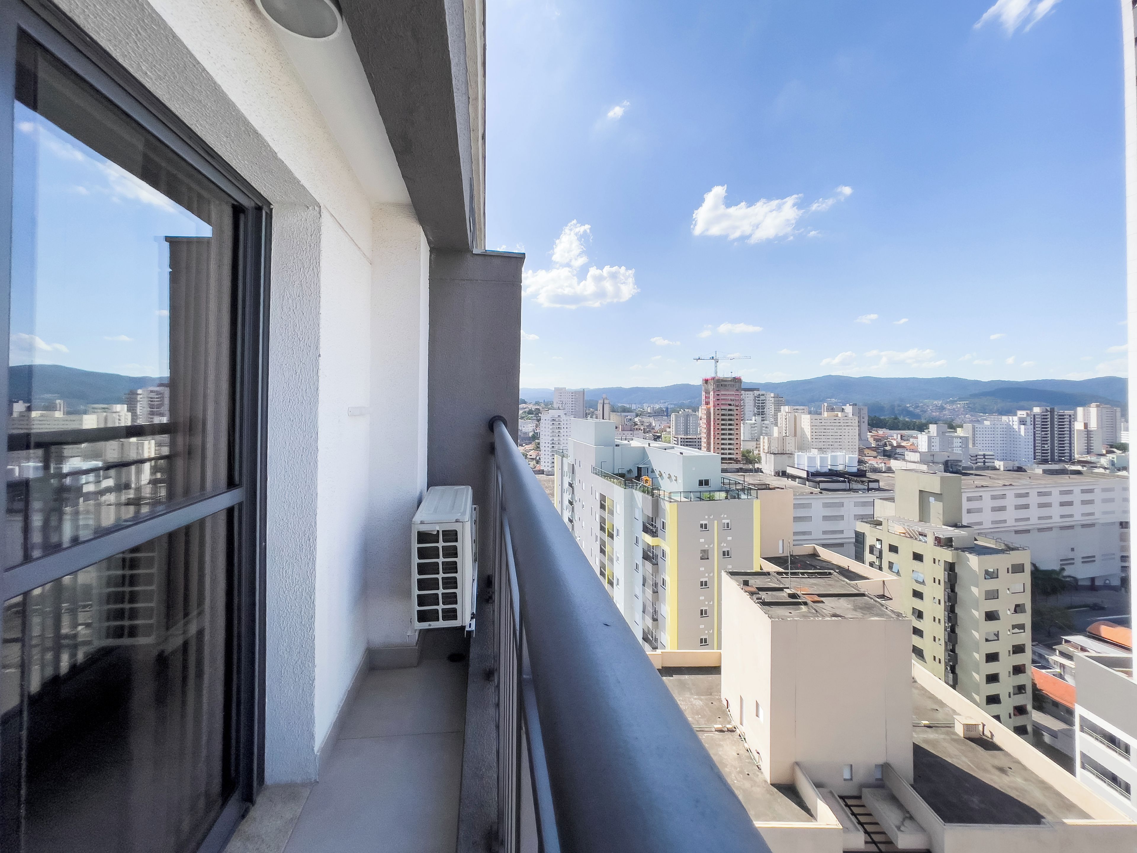 A balcony with a view of a cityscape, including buildings and mountains in the distance.
