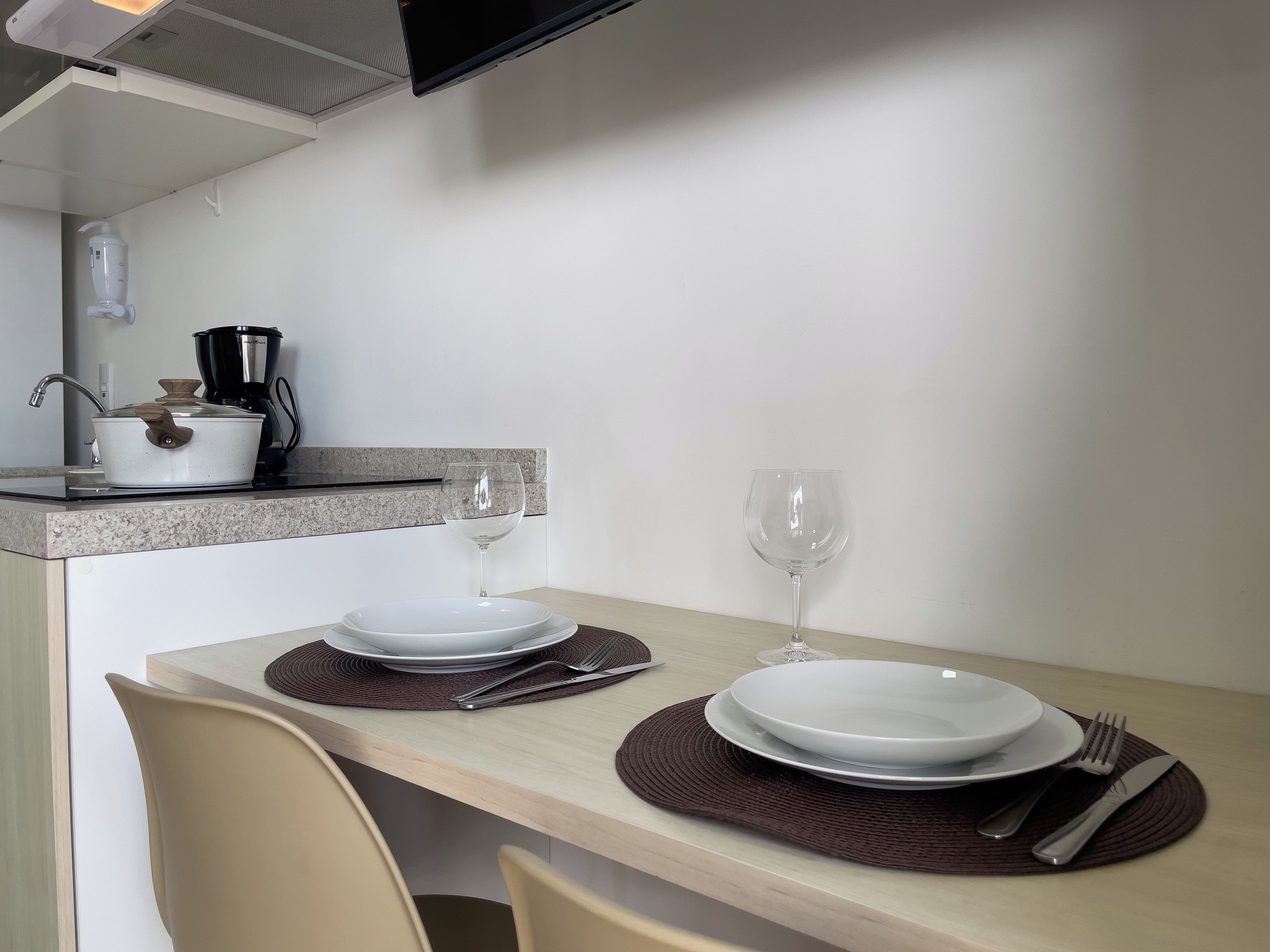 Un espace de restauration propre et moderne, avec une table dressée pour deux personnes, comprenant des assiettes, des couverts et un verre à vin.