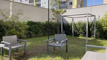 Un espacio al aire libre con dos sillas y un columpio, rodeado de vegetación y un edificio al fondo.