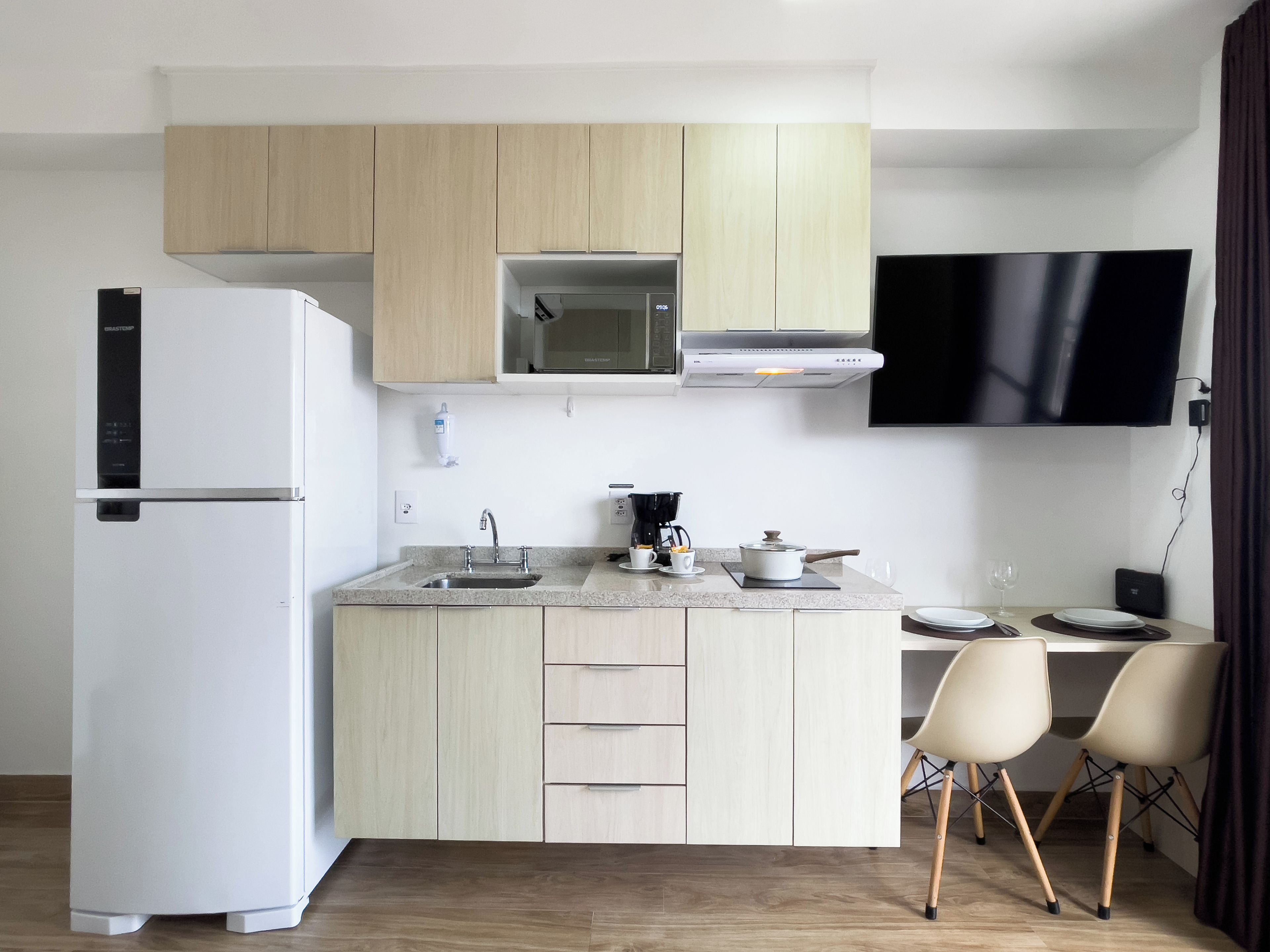A modern kitchen with a built-in microwave, a refrigerator, and a dining area with two chairs.