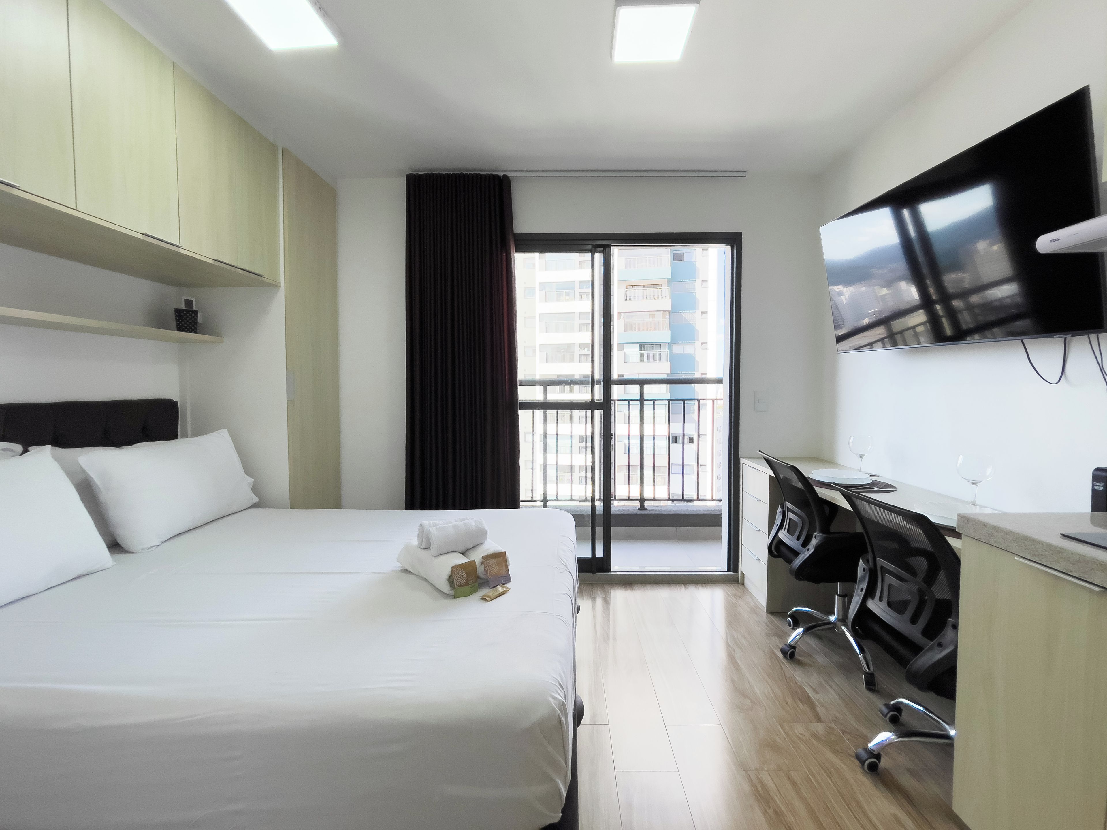 Une chambre d’hôtel équipée d’un lit, d’un bureau, d’une chaise, d’une télévision et offrant une vue sur la ville par la fenêtre.