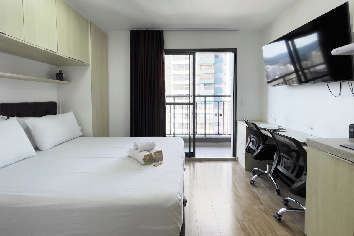 Ein Hotelzimmer mit Bett, Schreibtisch, Stuhl, Fernseher und Blick auf die Stadt durch ein Fenster.