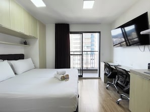 Ein Hotelzimmer mit Bett, Schreibtisch, Stuhl, Fernseher und Blick auf die Stadt durch ein Fenster.