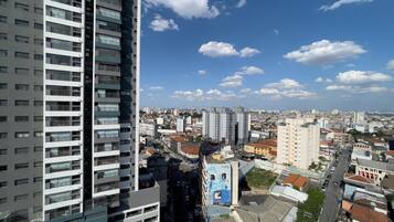 Un edificio de gran altura con varios pisos y balcones, un cielo azul despejado con algunas nubes, y una zona urbana densamente poblada con diferentes edificios y calles.