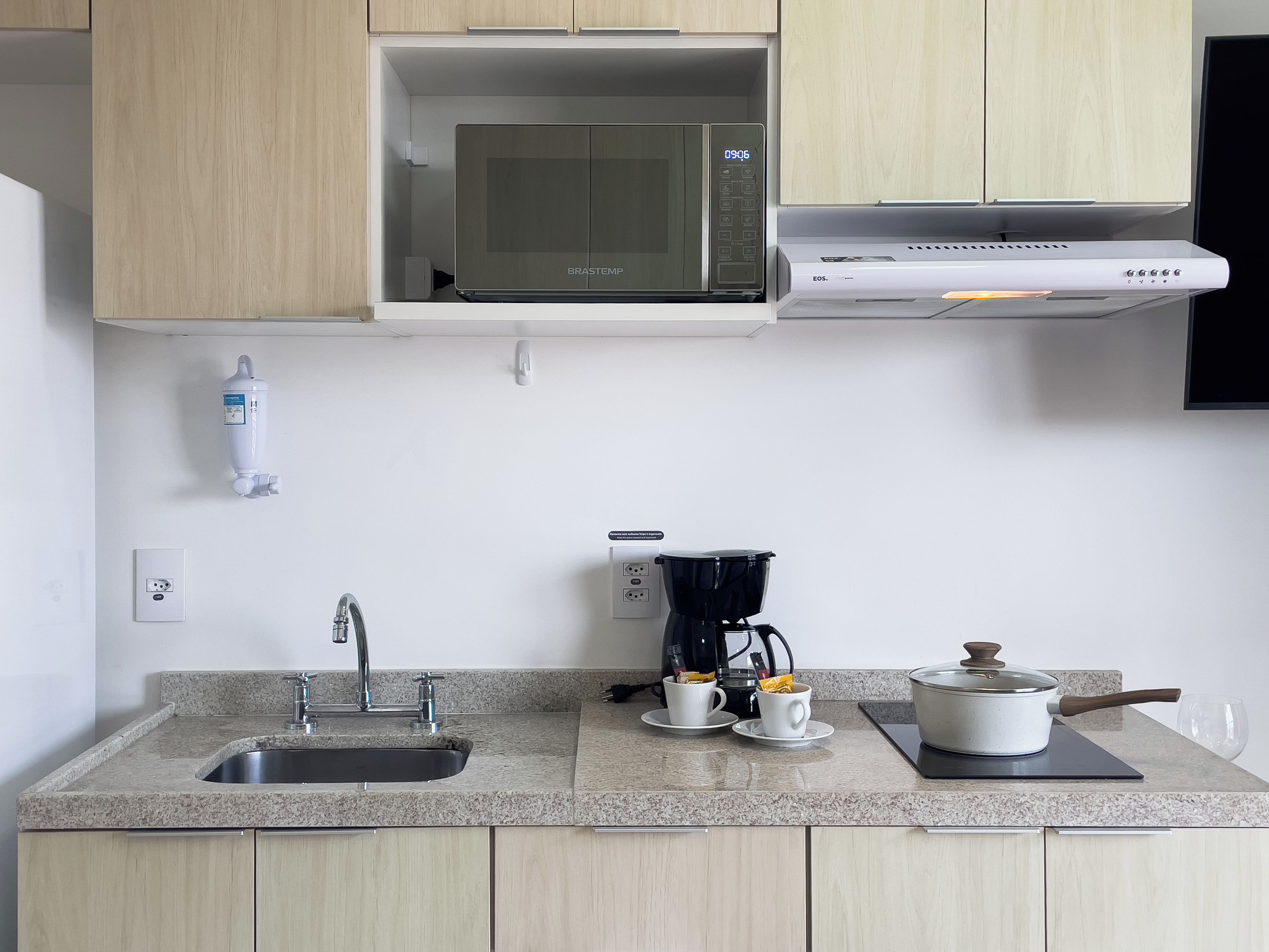 A kitchen with a built-in microwave, coffee maker, and a pot on the countertop.