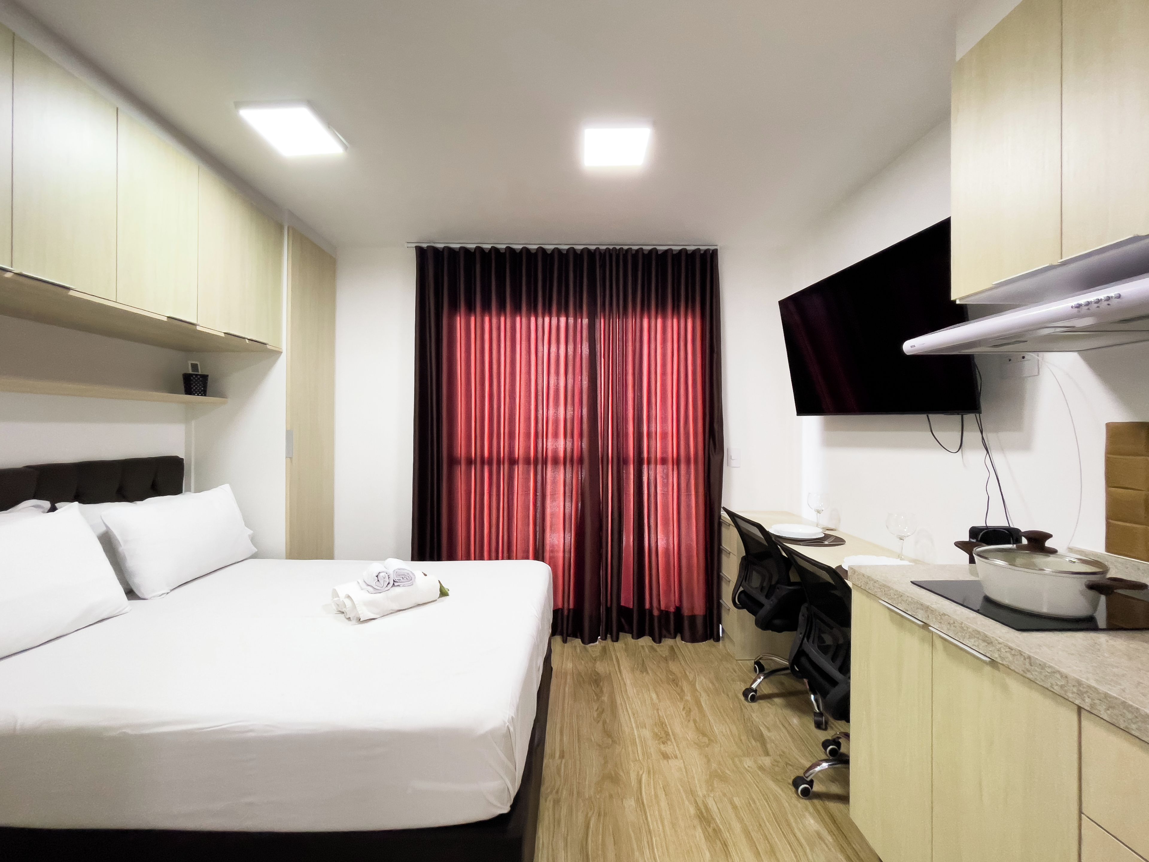Habitación de hotel con cama, escritorio, televisor de pantalla plana y kitchenette.