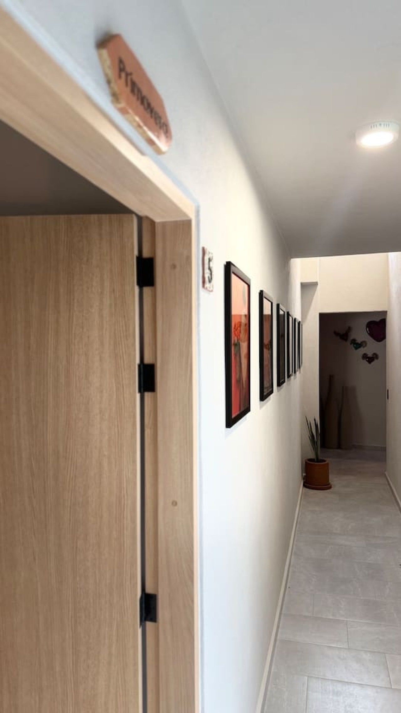A hallway with a wooden door, a sign above it, and a row of framed pictures on the wall.