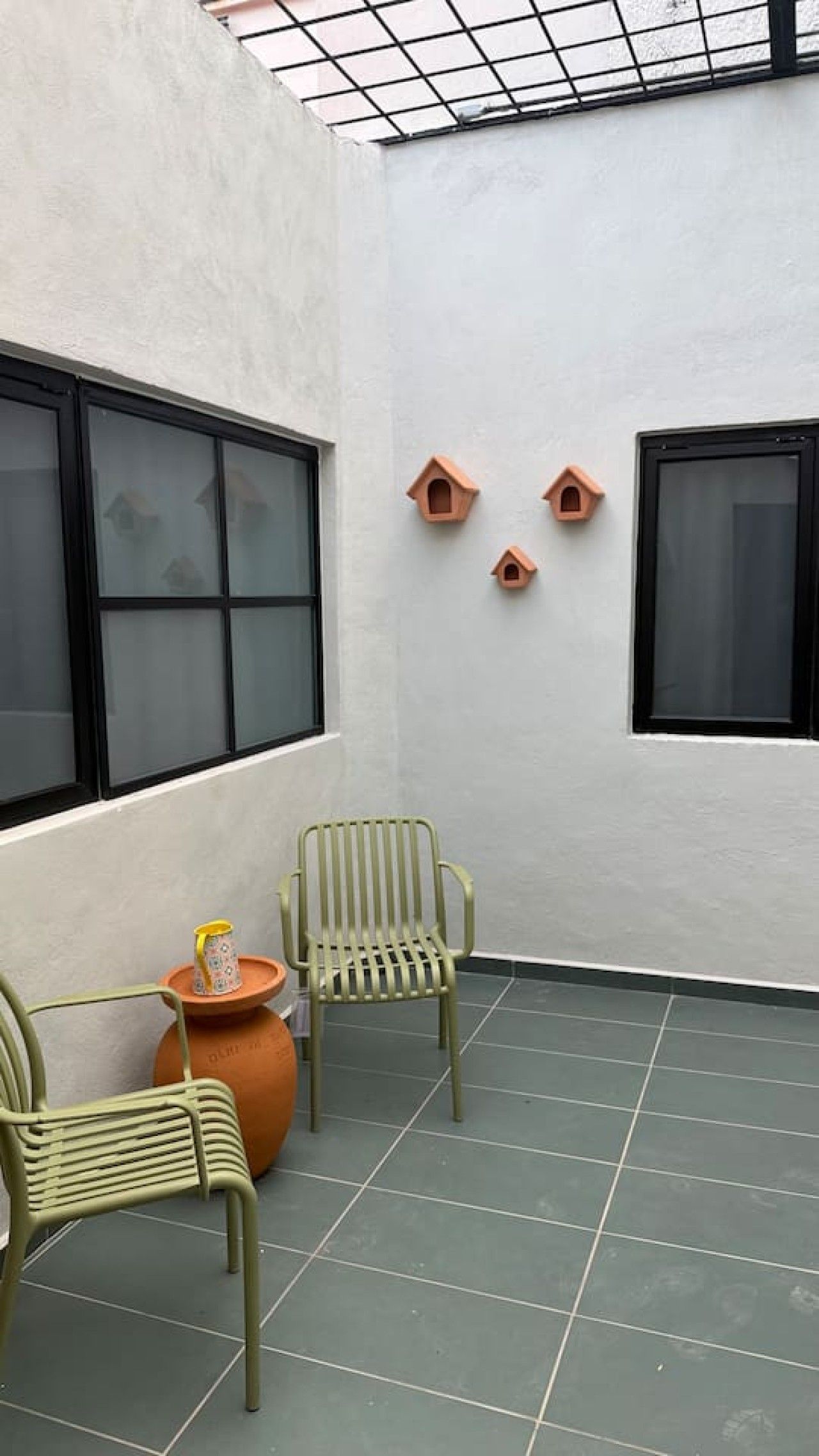 A room with two green chairs, a small table, and two birdhouse decorations on the wall.