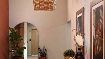 A hallway with a woven light fixture, potted plants, a wooden bench, and framed artwork on the walls.