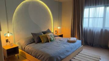 A modern bedroom with a large bed, two bedside tables, a nightstand, a wall arch, and a window with curtains.