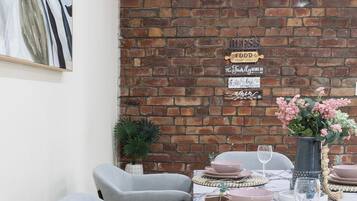 A dining area with a brick wall, a marble table, grey chairs, and a vase with flowers.