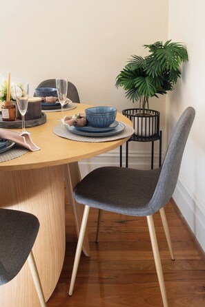 A dining table with a blue bowl, two glasses, and a candle. There are chairs with grey upholstery and a potted plant beside the table. - Historic 4BR Edwardian Terrace | Walk to Rail (Redfern)