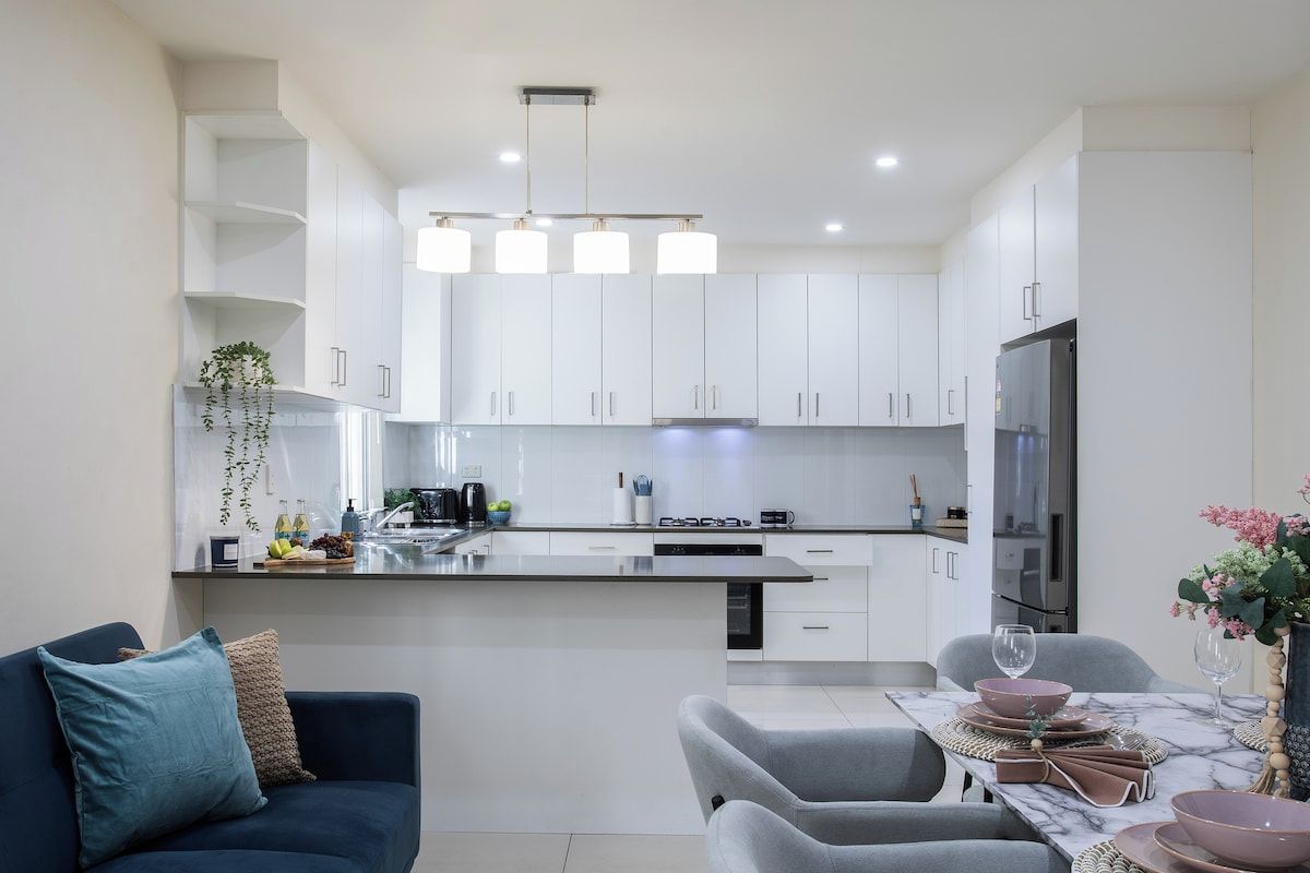A modern kitchen with white cabinets, a central island, and a dining area with grey chairs and a table.