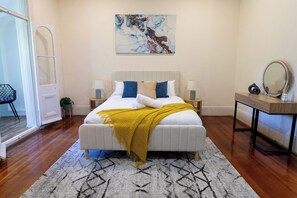 A bedroom with a bed, bedside tables, a mirror, a painting, and a door. - Historic 4BR Edwardian Terrace | Walk to Rail (Redfern)