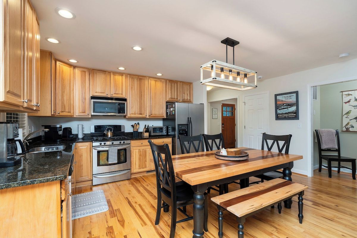 A modern kitchen with wooden cabinets, stainless steel appliances, and a wooden dining table with chairs.