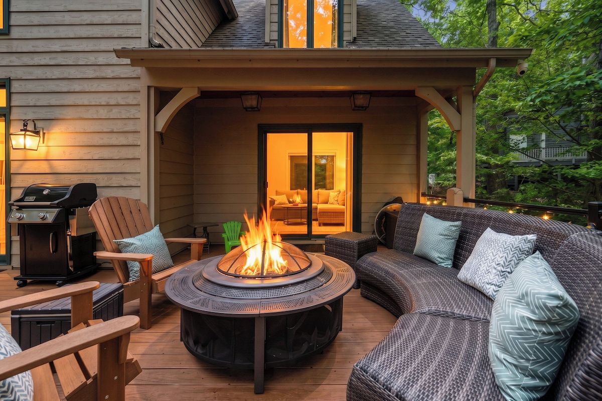 A covered outdoor seating area with a fire pit, a grill, and a sofa with cushions.