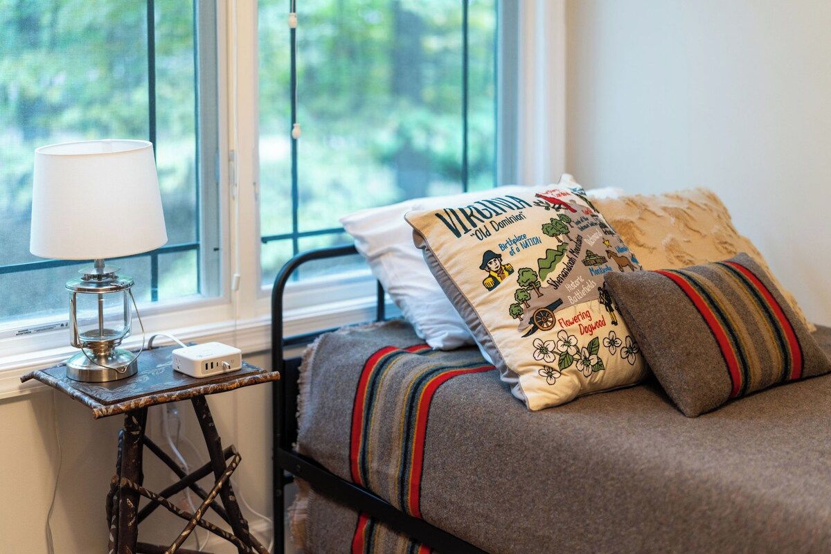 A bed with a striped blanket, a lamp, and a pillow with a nature-themed design.