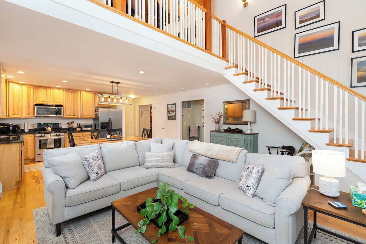 A spacious living area with a large sectional sofa, a coffee table with a plant, and a staircase with a railing.