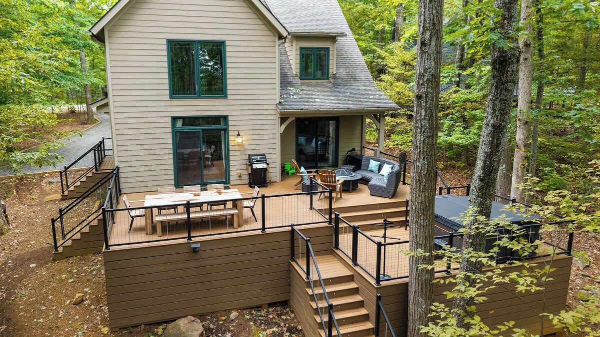 A two-story house with a deck, outdoor seating, and a grill.