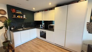 A modern kitchen with white cabinets, a black countertop, and a microwave. - Serene 1BDR Brixton Retreat with Private Patio (Greater London)