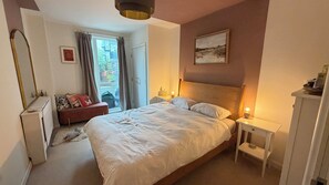 Quarto com cama, mesas de cabeceira, um radiador, um espelho e um quadro na parede.