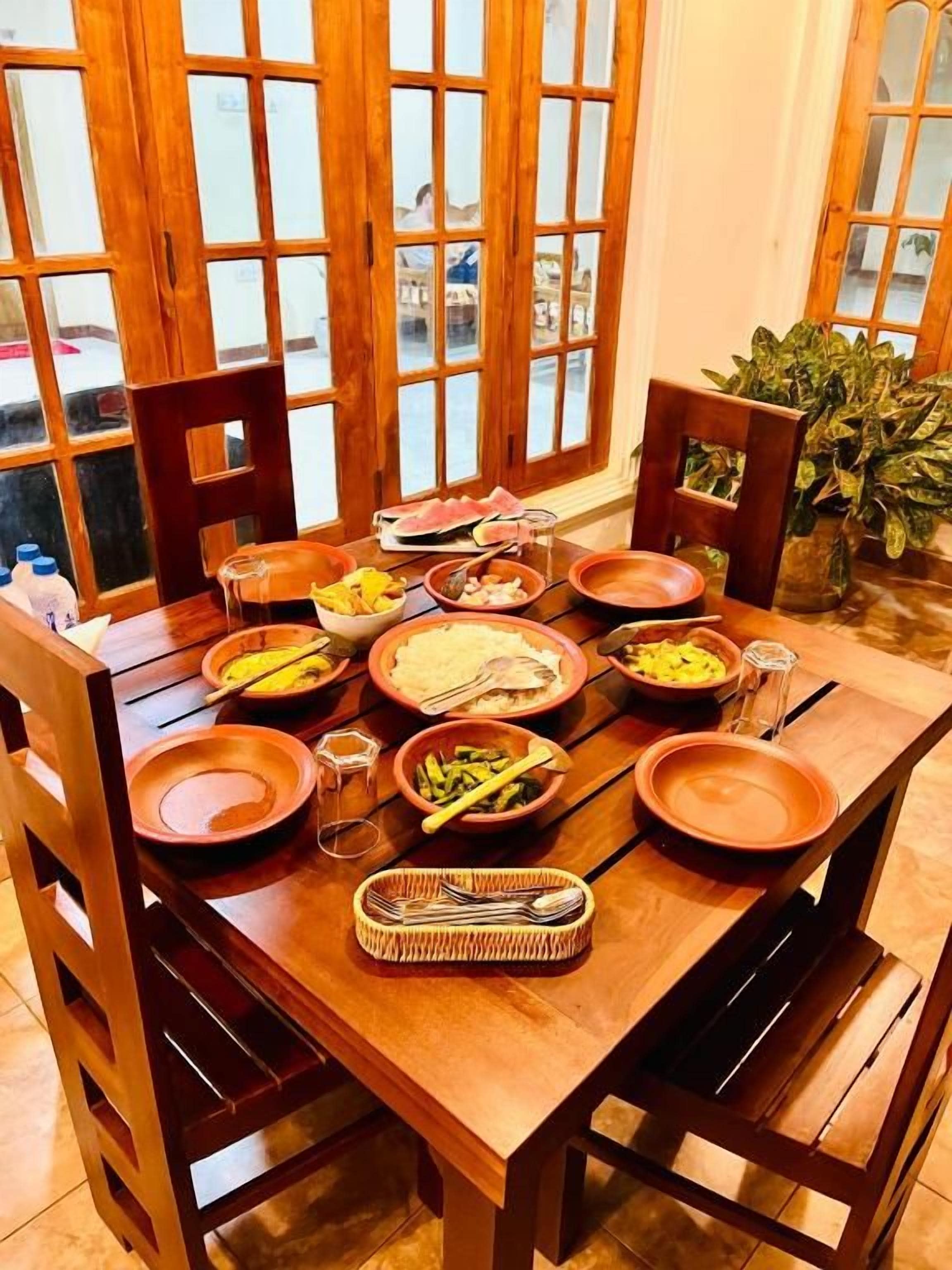 A wooden dining table set with plates, bowls, and utensils, surrounded by chairs.