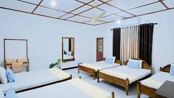 A hotel room with four single beds, a wooden table, a ceiling fan, and a large window with curtains.