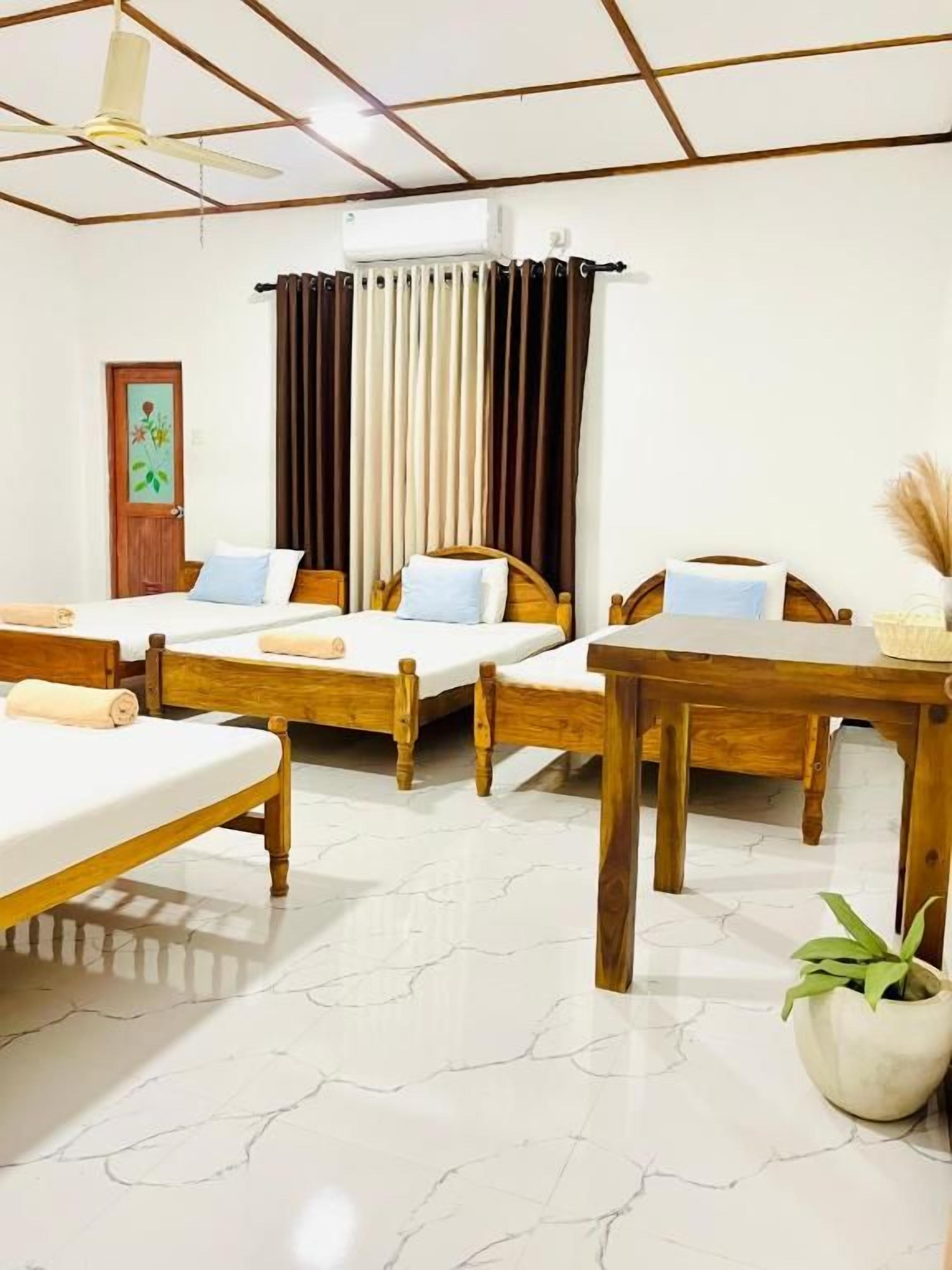 Une chambre d’hôtel avec quatre lits, un ventilateur de plafond, un appareil de climatisation et une plante en pot.