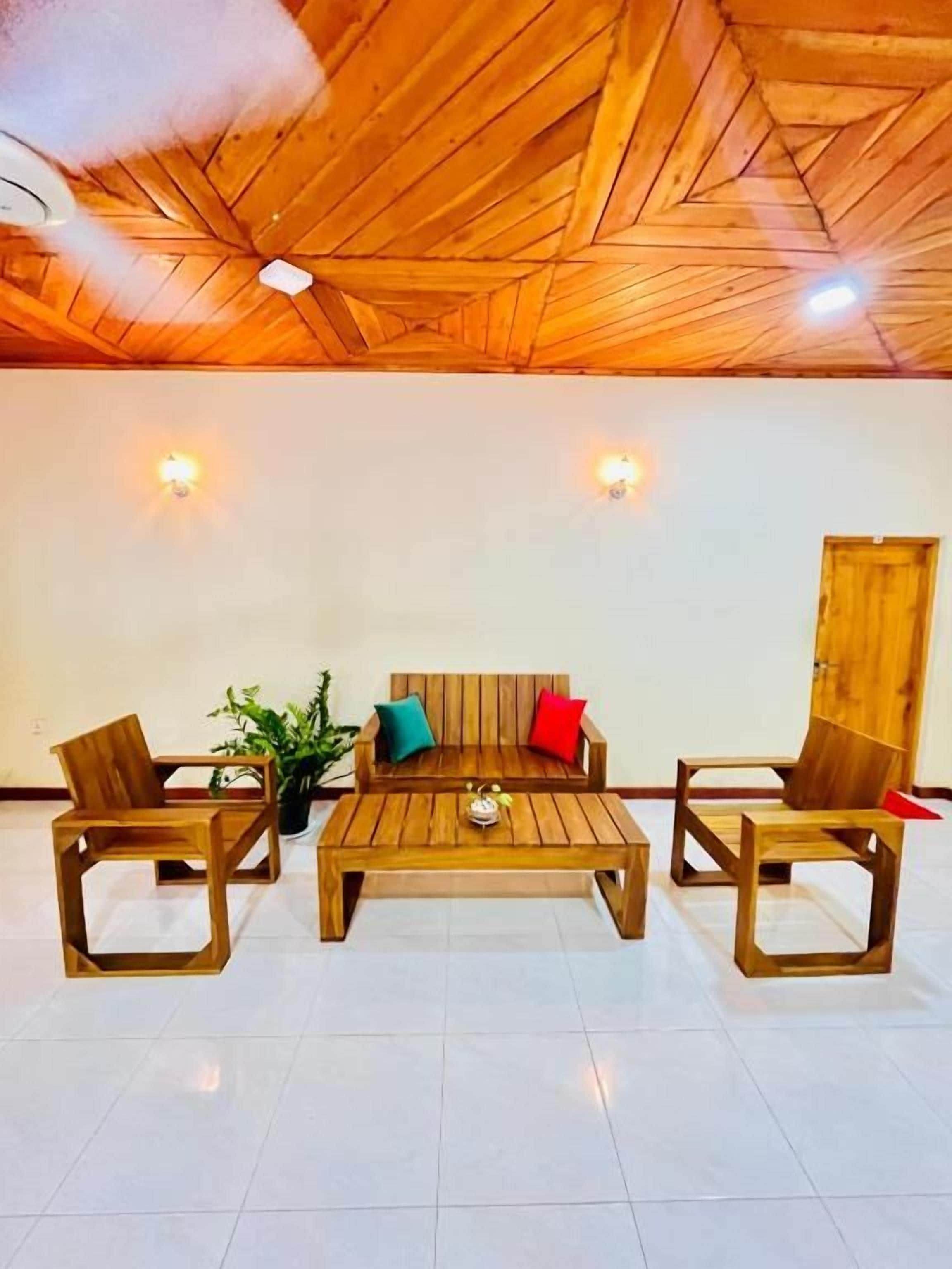 A room with a wooden ceiling, a sofa set, two chairs, a coffee table, and wall-mounted lights.