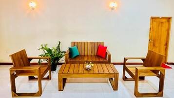 A room with a wooden ceiling, a sofa set, two chairs, a coffee table, and wall-mounted lights.