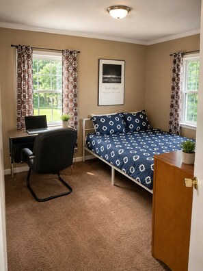 Ein Schlafzimmer mit einem Bett, einem Schreibtisch mit Laptop, einem Stuhl und einer Tür.