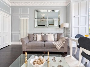 A modern living room with a grey sofa, a glass coffee table with decorative items, a lamp, and a chair. - Charming 3BR - Stockbridge & Botanic Garden (Edinburgh)