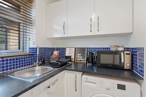A kitchen with a sink, a microwave, a coffee maker, and a framed sign. - The Hideaway - Perfect for professionals, contractors and leisure guests (Ash Vale)