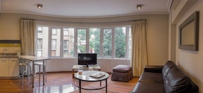 A modern living room with a flat-screen TV, a dining area with a bar, and large windows offering a view of the city. - Luxury 1-Bedroom Apartment in Lastarria (Santiago)