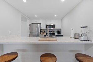 A modern kitchen with white cabinetry, stainless steel appliances, a marble countertop, and wooden bar stools. - 🏖️ Beautiful Bay Views | Close to Beach | Pool | Dockside Paradise 🐬 (Fort Myers Beach)