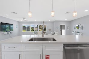 Una cocina moderna con una isla central, armarios blancos y un lavaplatos de acero inoxidable.