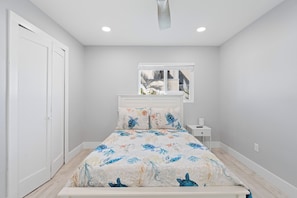 A bedroom with a bed, a nightstand, a window, and a door. - Beachside Oasis 🌴 Canal Front 4BR Home | Private Pool + Spillover Spa (Fort Myers Beach)